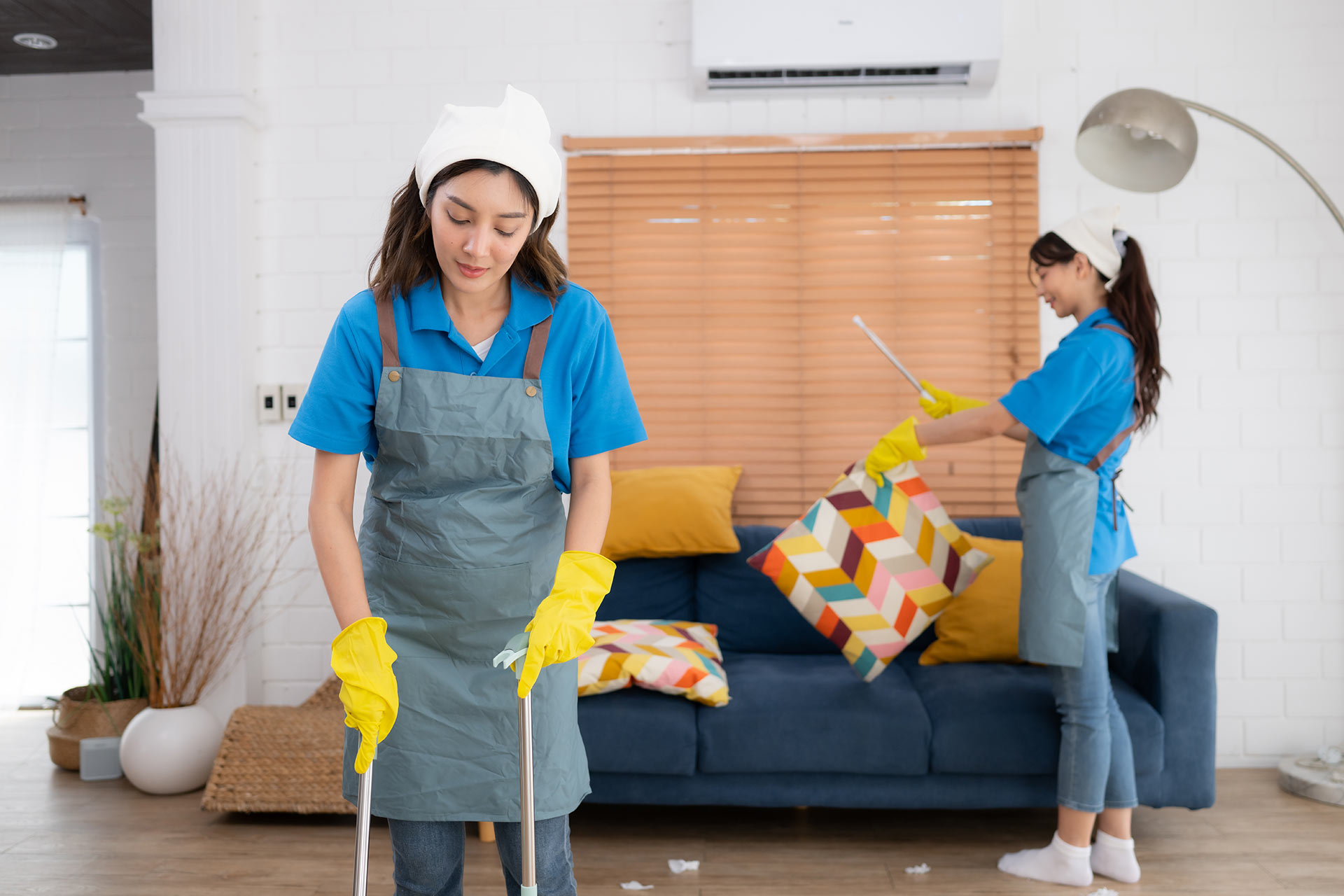 Two women diligently cleaning a room featuring a couch and a chair, showcasing teamwork and attention to detail.