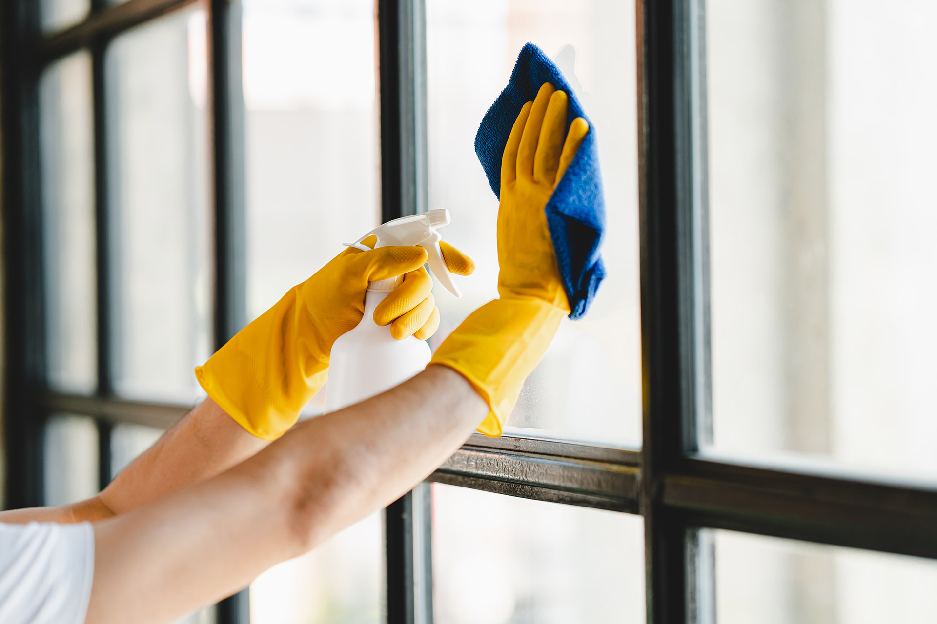 A person wearing a yellow glove is diligently cleaning a window, ensuring a clear and spotless surface.